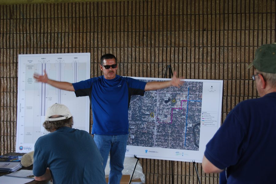 Mark McNeal presenting a well cross-section and an aerial site map to a seated group