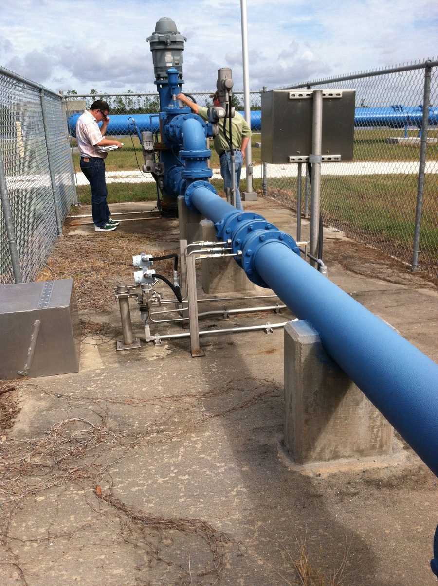 Two people working at a potable ASR wellhead, blue above-ground pipework and valves